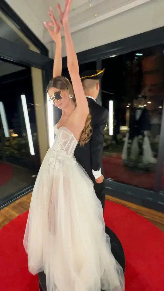 Panna młoda w białej sukni i okularach przeciwsłonecznych na platformie fotobudki 360, za nią pan młody